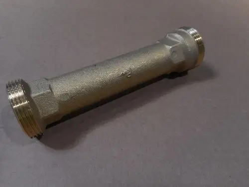 Remeha Rücklaufrohr in zylindrischer Form, mit Gewinde an beiden Enden, auf grauem Hintergrund liegend.